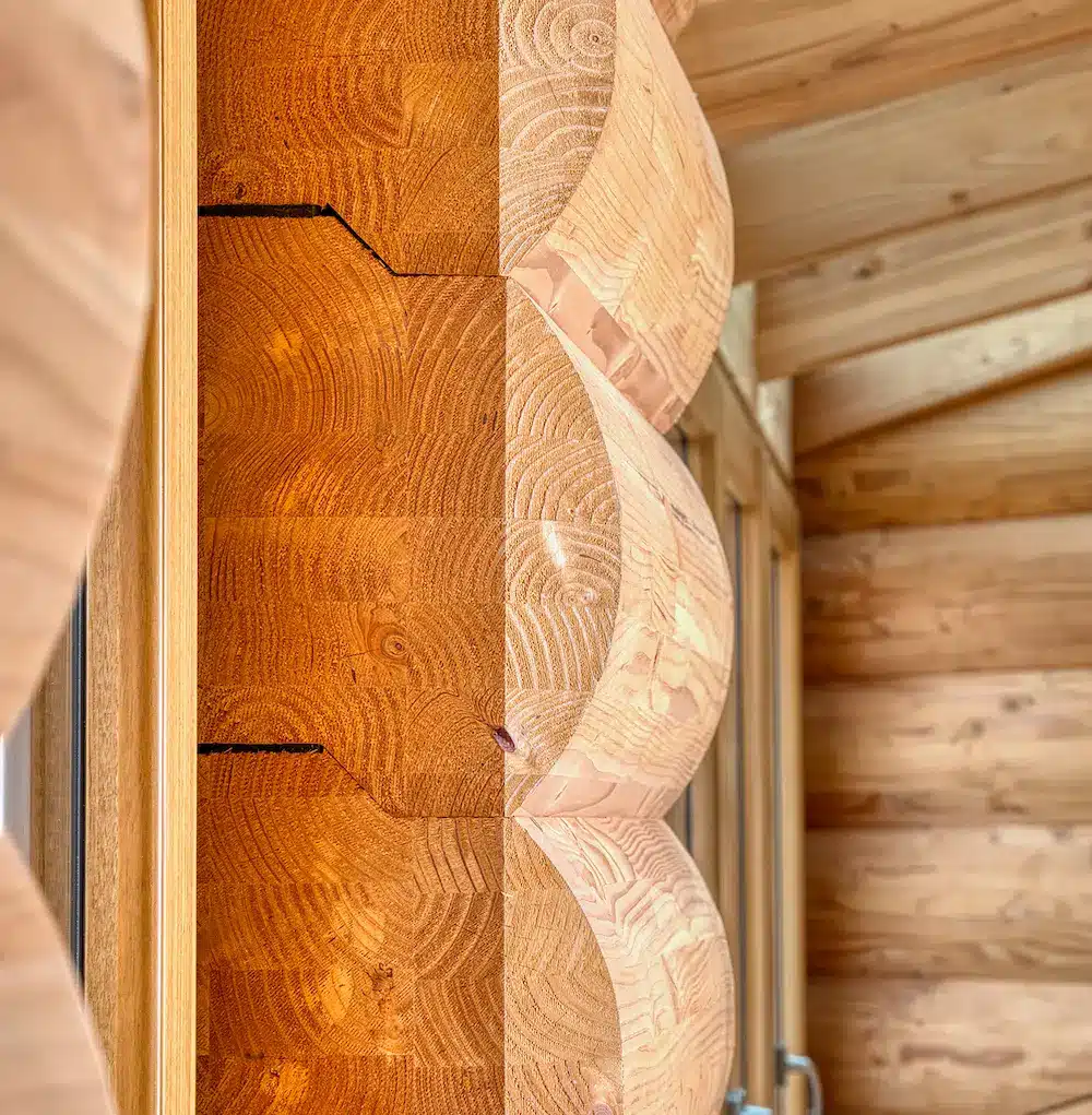 MONOLOG, détail constructif de maison en rondins: assemblage près d’une fenêtre, veinage du bois et intérieur bois.